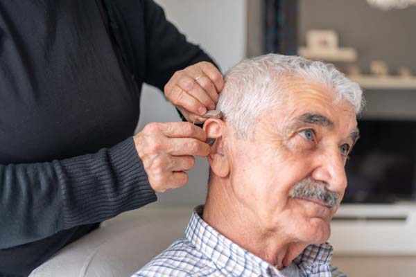 Caregiver Inserting Hearing Aid In Senior's Ear